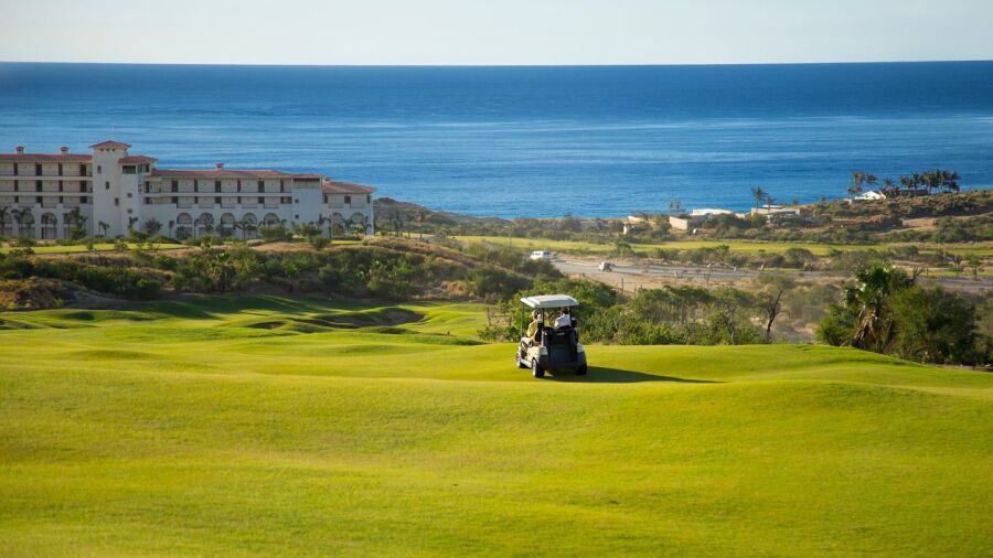Golf cart on a Los Cabos golf course with resort buildings and the Sea of Cortez in the background